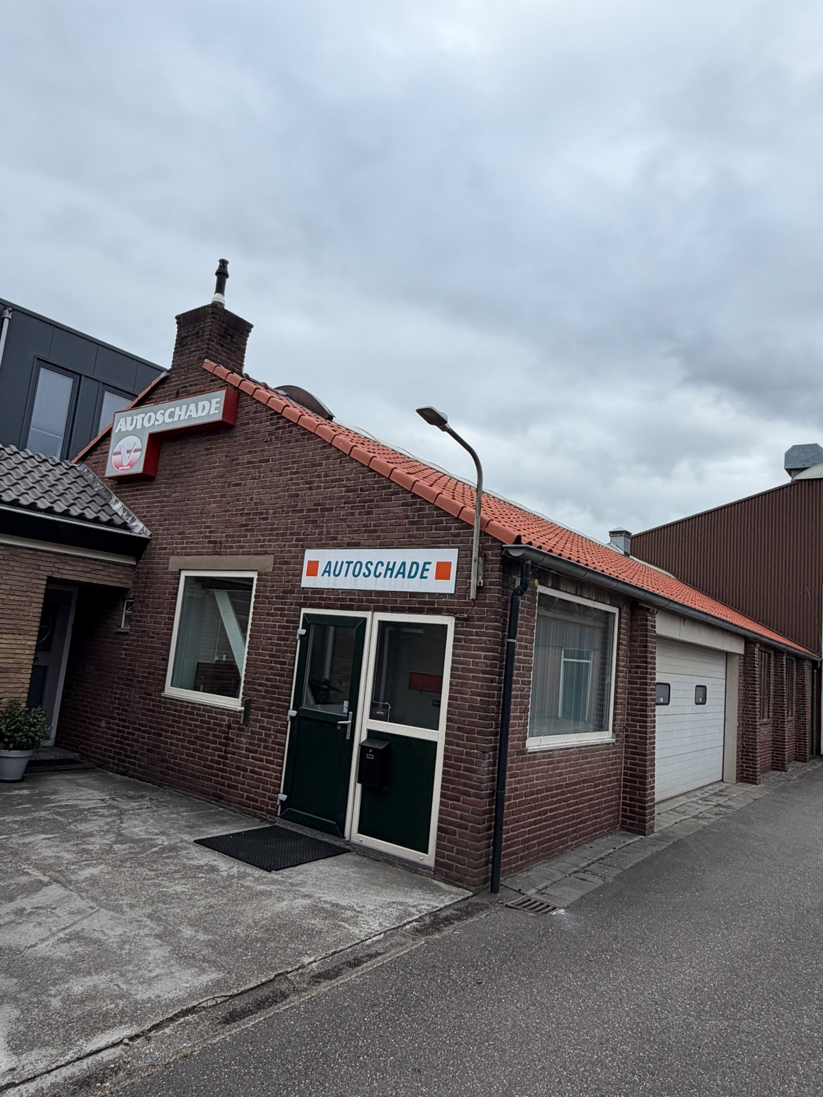De bakstenen gevel van DuPau met het bord Autoschade en de groene toegangsdeur
